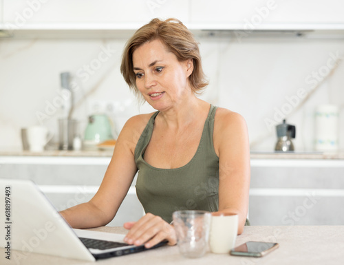 Smiling woman working remotely on laptop at table in kitchen at home