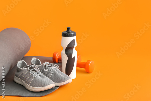 Yoga mat with sports bottle, dumbbells and sneakers on orange background photo