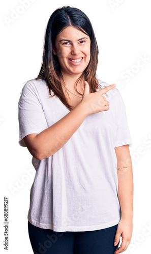 Young beautiful brunette woman wearing casual t-shirt cheerful with a smile of face pointing with hand and finger up to the side with happy and natural expression on face © Krakenimages.com