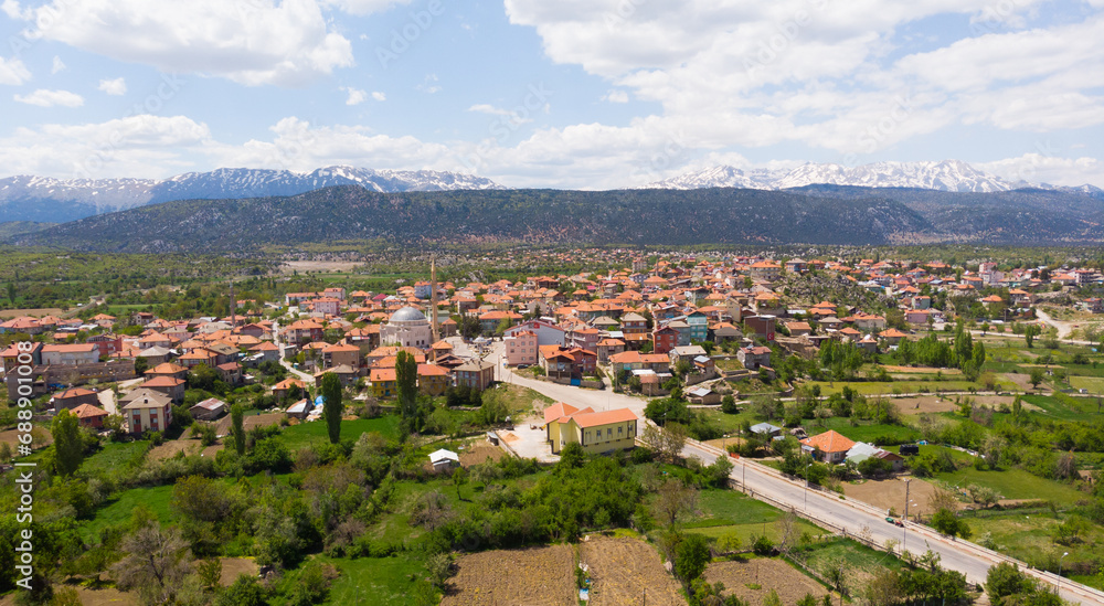 Scenic spring view from drone of Yesildag village with residential houses and mosque in green valley surrounded by mountains with peaks covered with snow, Turkey