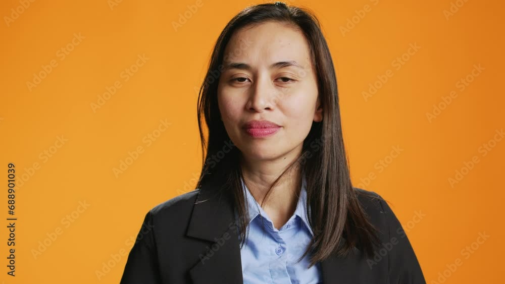 Filipino person shows hush gesture on camera, doing mute sign to keep secret and be private. Woman putting finger over lips for silence, asking for secrecy against orange background. Filipino person shows hush gesture on camera, doing mute sign to keep secret and be private. Woman putting finger over lips for silence, asking for secrecy against orange background.