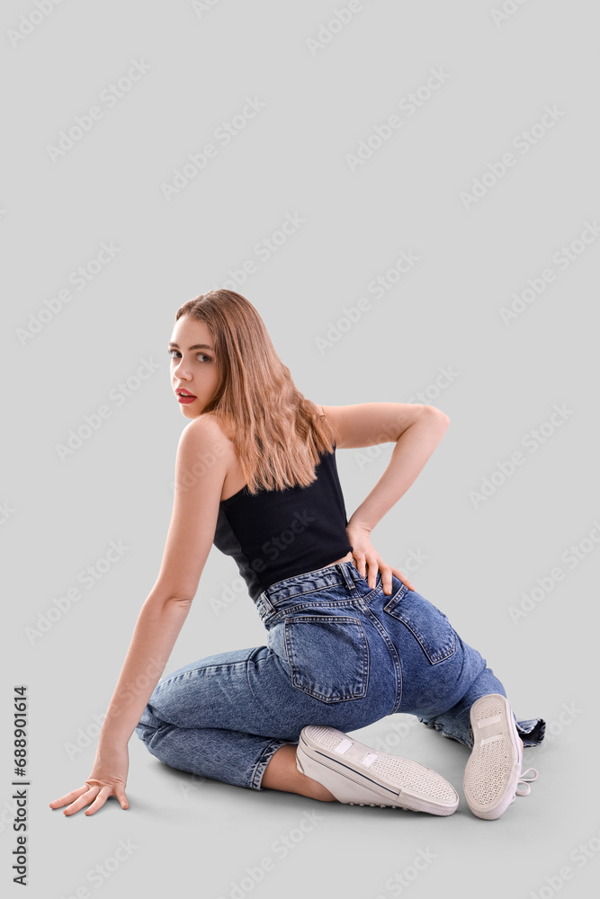 Young woman in dark blue jeans on light background, back view