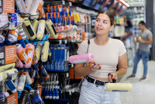 Young smiling woman buying tools for house decoration in paint supplies store © JackF