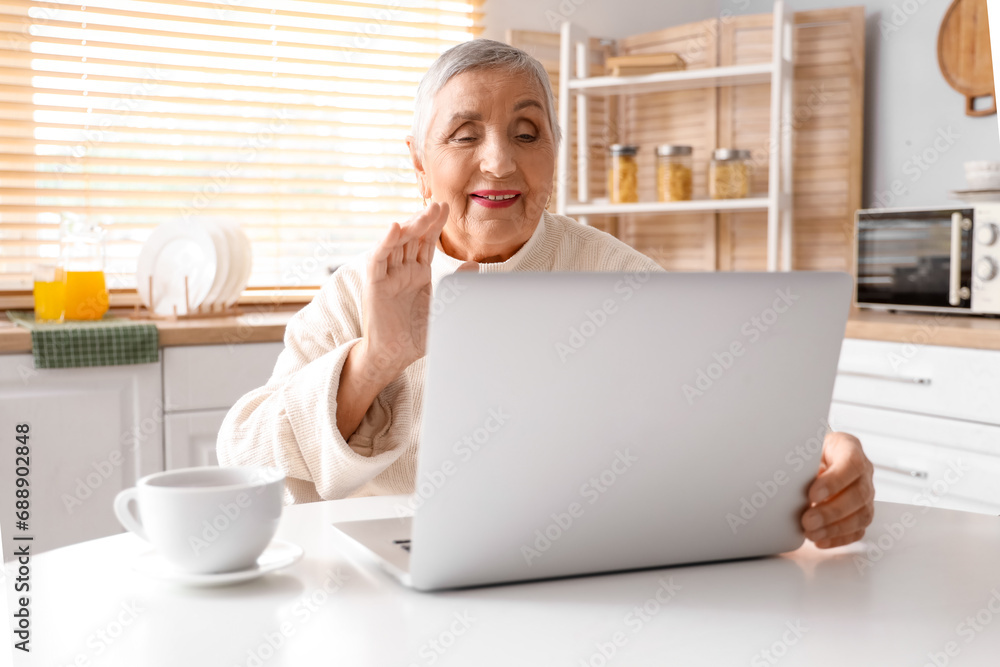 Senior woman with laptop video chatting at table in kitchen Senior woman with laptop video chatting at table in kitchen
