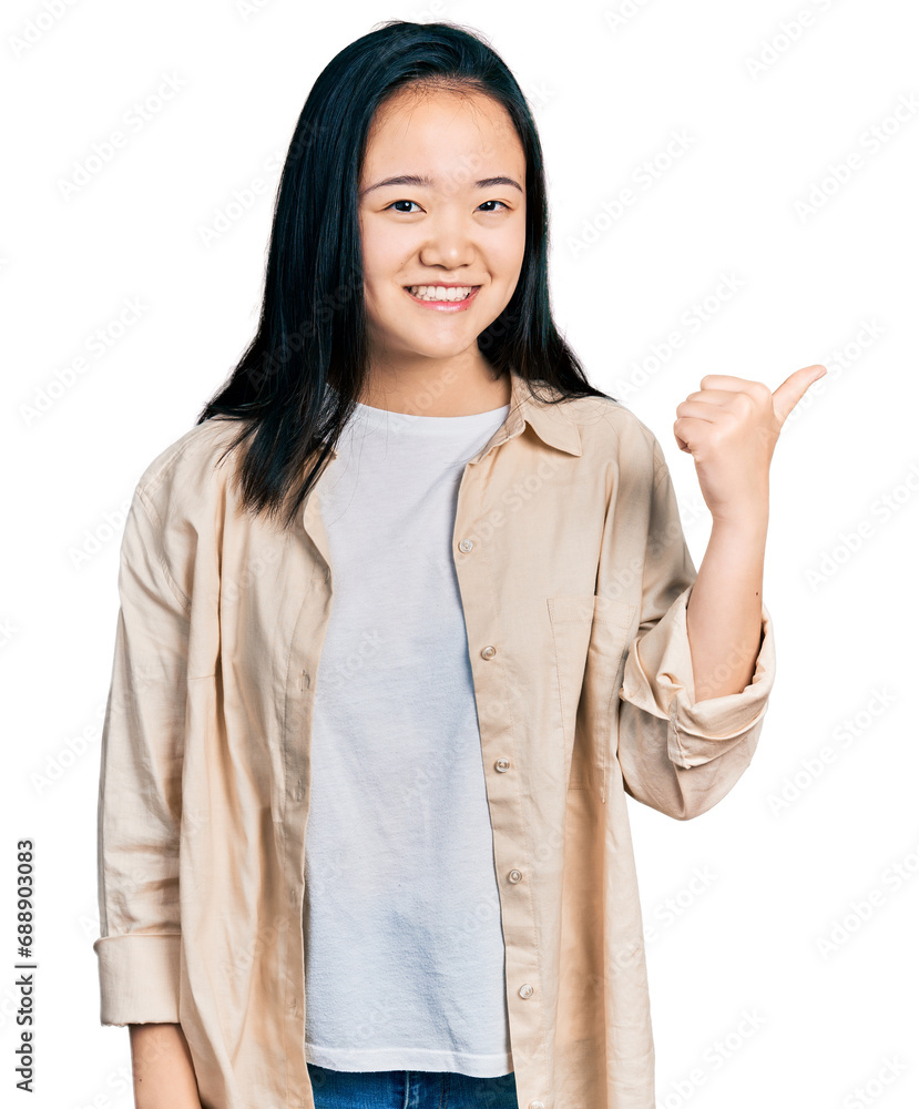 Young chinese woman wearing casual white t shirt and jacket smiling with happy face looking and pointing to the side with thumb up. Young chinese woman wearing casual white t shirt and jacket smiling with happy face looking and pointing to the side with thumb up.