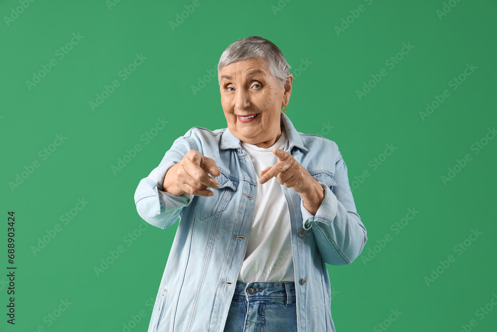 Senior woman pointing at viewer on green background Senior woman pointing at viewer on green background