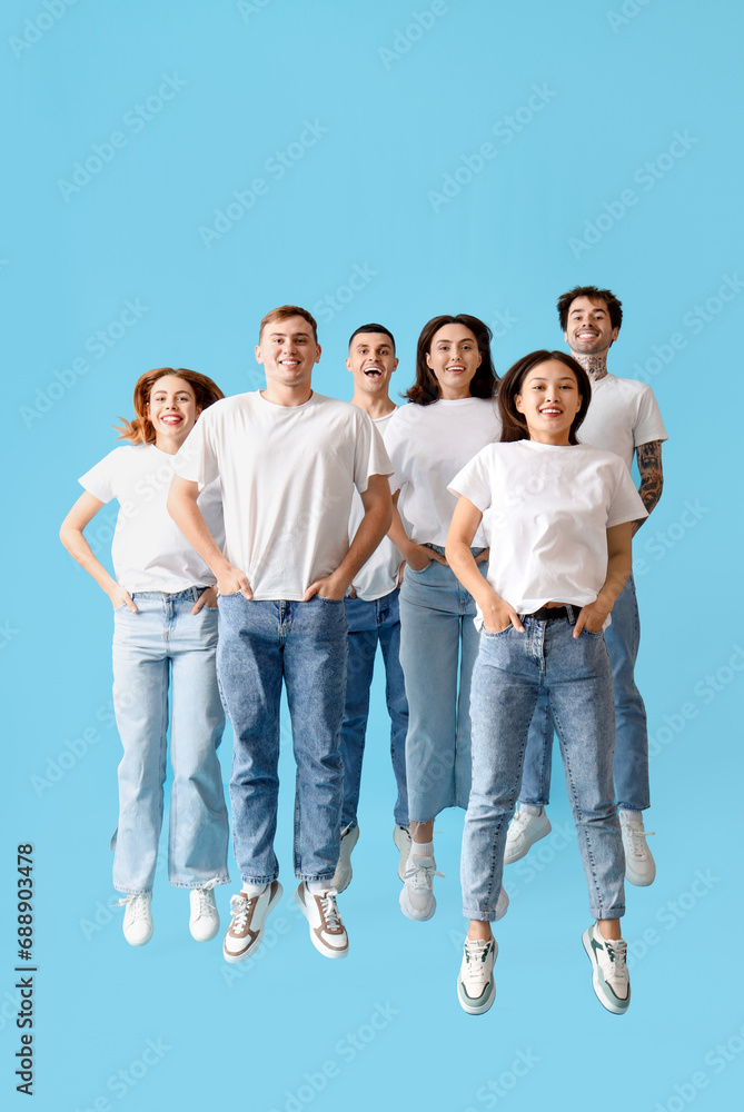 Group of young people in stylish jeans jumping on blue background
