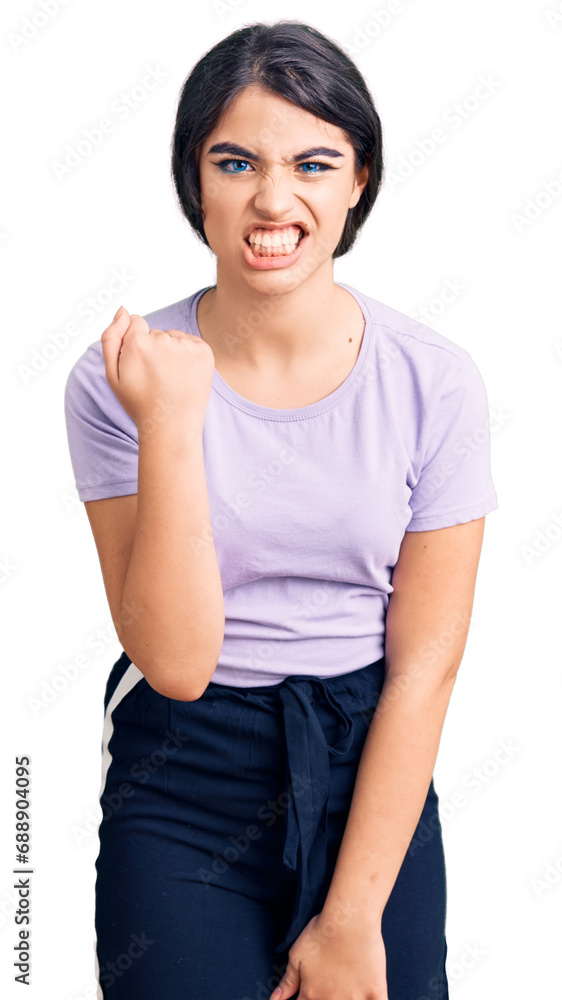 Brunette teenager girl wearing casual clothes angry and mad raising fist frustrated and furious while shouting with anger. rage and aggressive concept. Brunette teenager girl wearing casual clothes angry and mad raising fist frustrated and furious while shouting with anger. rage and aggressive concept.