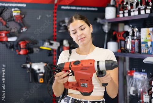 Woman examines tool and buys electric perforator, collects supplies in store according to list for apartment renovations. Construction items, paint and varnish products, accessories, supermarket