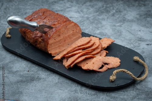 Vegan meat alternative- seitan  made with gluten and tofu, seasoned with spices, glazed with BBQ sauce. White plate, sliced, slate board