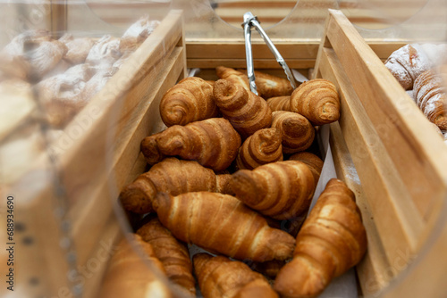 Lots of fresh croissants on a wooden counter in a store. Delicious crispy pastry for breakfast. Close-up.
