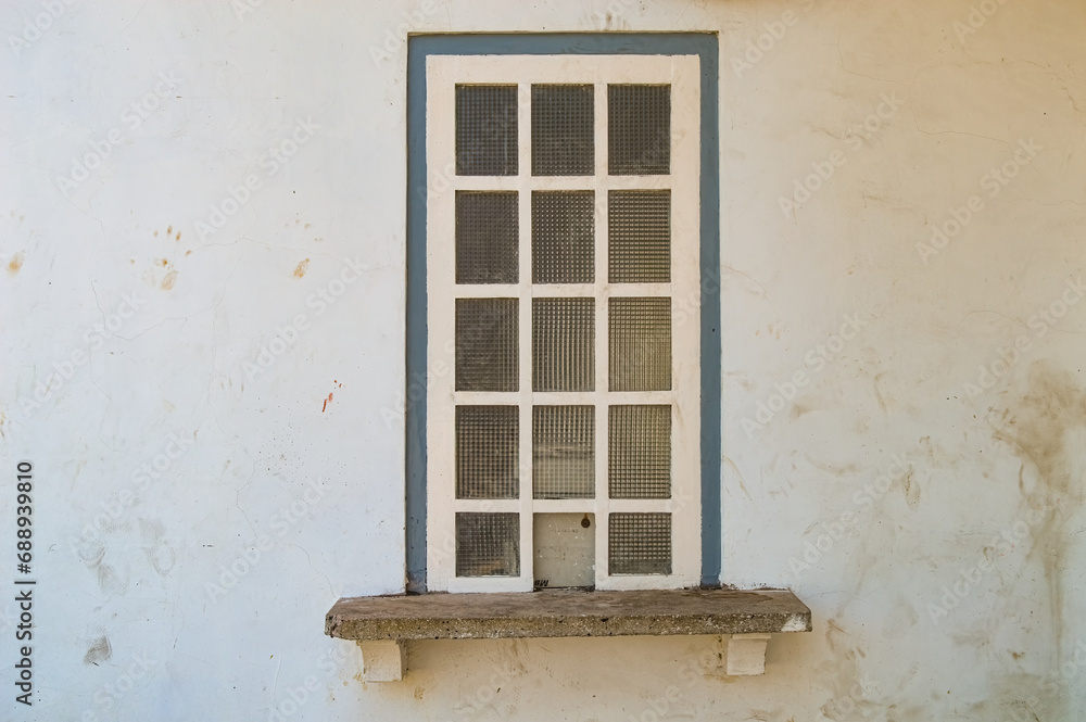 a white Greek-style wooden window that was previously used as a counter in an old building that is now no longer used