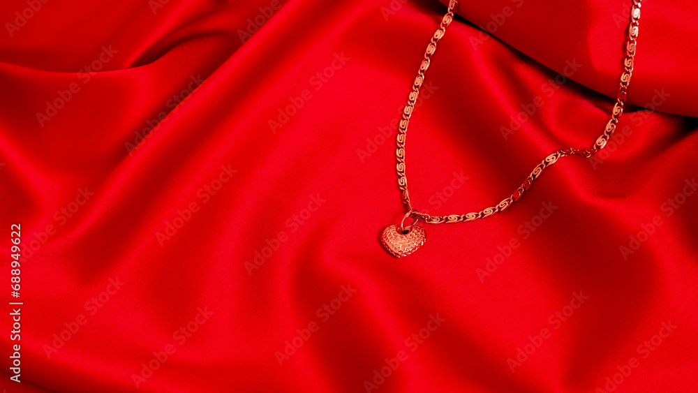 Gold chain with a pendant in the form of a heart on a red satin background. Luxury women's jewelry, close-up. Banner Gold chain with a pendant in the form of a heart on a red satin background. Luxury women's jewelry, close-up. Banner