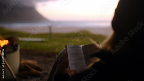 Person, camping and sunset with reading book, travel and back on holiday by the beach an coast. Calm, relax and ocean with adventure trip and vacation outdoor with sunrise and freedom in nature photo