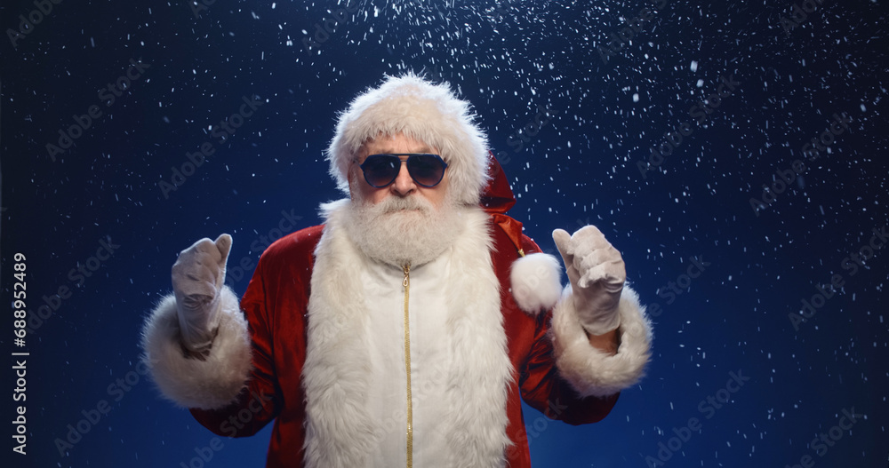 Cool santa claus wearing sunglasses dancing to music, isolated over snowy blue background - christmas party, christmas spirit concept close up Cool santa claus wearing sunglasses dancing to music, isolated over snowy blue background - christmas party, christmas spirit concept close up