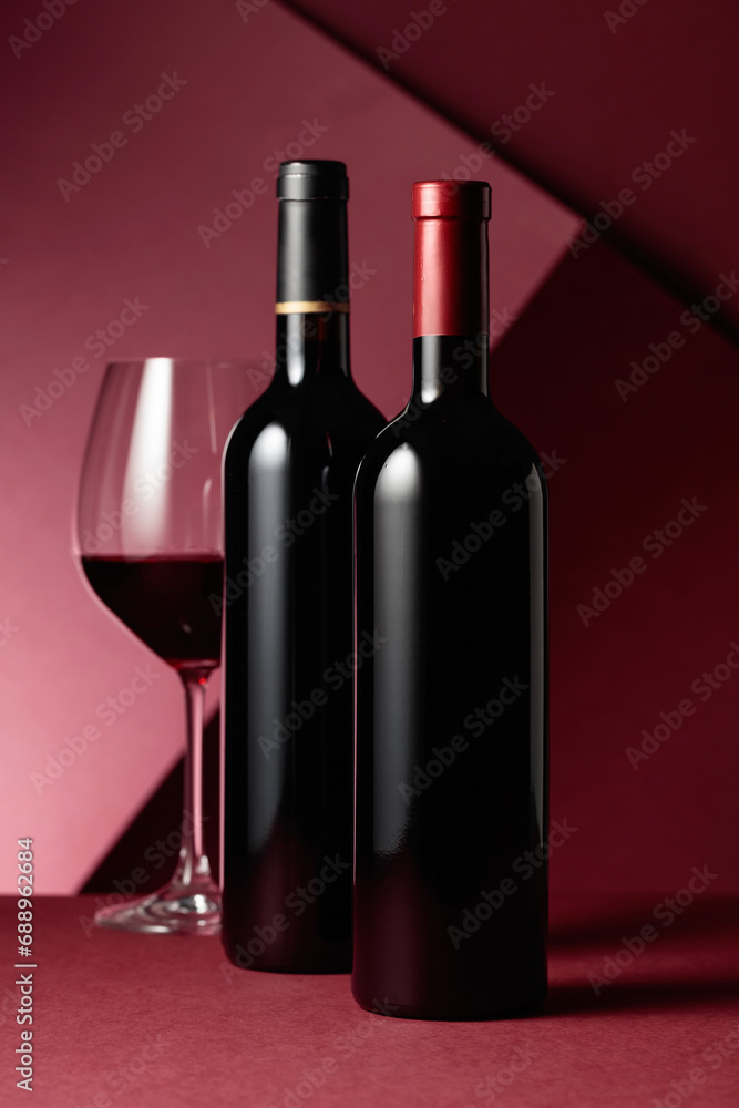 Fototapeta premium Glass and bottles of red wine on a red background.