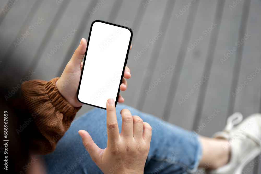 Close-up image of a woman in casual clothes sitting outdoors in the city and using her smartphone. Close-up image of a woman in casual clothes sitting outdoors in the city and using her smartphone.