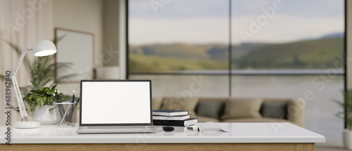 Close-up image of a white-screen laptop mockup on a white tabletop in a modern spacious living room.