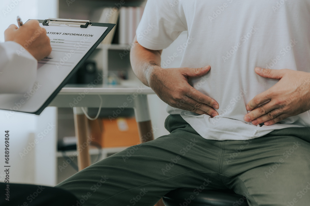 Crohn's disease or ulcerative colitis concept. Doctor counseling male patient with abdominal pain in hospital examination room - obrazy, fototapety, plakaty 