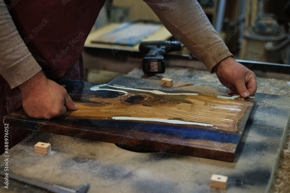 The focus and precision of a carpenter are evident as he sands down a wooden board, immersed in the process of shaping and finishing.