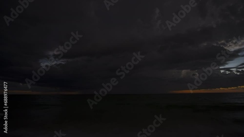 Time-lapse landscape of dark ominous rainstorm with lightning and thunder over sea water waves crushing on sandy beach. Beautiful seascape in evening photo