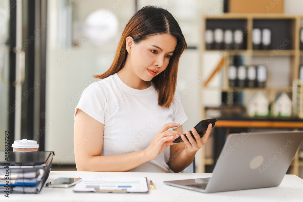 Cheerful Asian woman confidently uses mobile phone, tablet with laptop and notebooks on the desk in a bright office. Cheerful Asian woman confidently uses mobile phone, tablet with laptop and notebooks on the desk in a bright office.