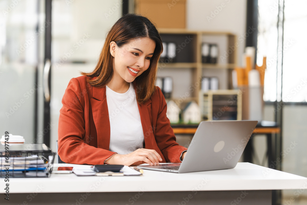 Middle-age attractive Asian insurance agent is focused on her laptop, working on asset management in a well-lit office environment. Middle-age attractive Asian insurance agent is focused on her laptop, working on asset management in a well-lit office environment.