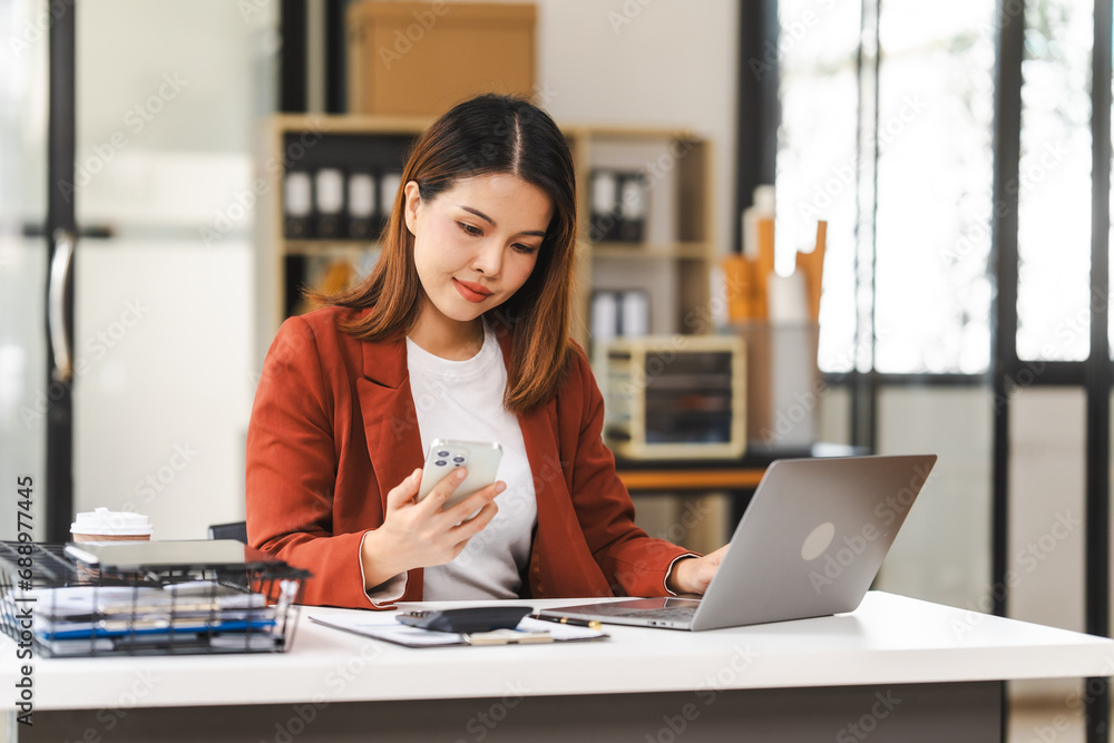 Fototapeta premium Middle-age attractive Asian insurance agent is focused on her laptop, working on asset management in a well-lit office environment.