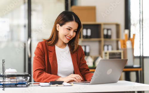 Middle-age attractive Asian insurance agent is focused on her laptop, working on asset management in a well-lit office environment.