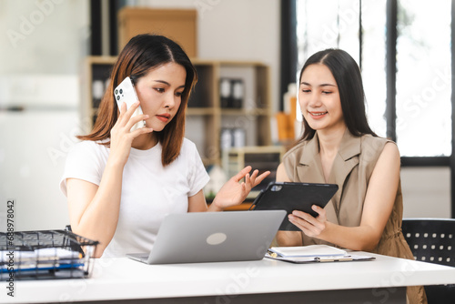 Two Asian colleagues, freelance writer and graphic designer discussing about creating characters in screenplays work and smiling with tablets and a laptop, journalist, artist, meeting together