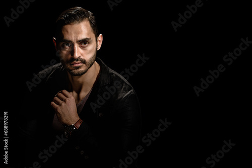 Portrait of young fashionable bearded man isolated on black background, Dramatic low-key portrait of a young man with a dark ambiance, showcasing his beard © Denys Kurbatov