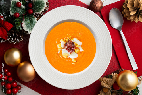 Traditional spanish salmorejo. Cold tomato soup served with egg and iberico jam. Christmas food served on a table decorated with Christmas motifs.