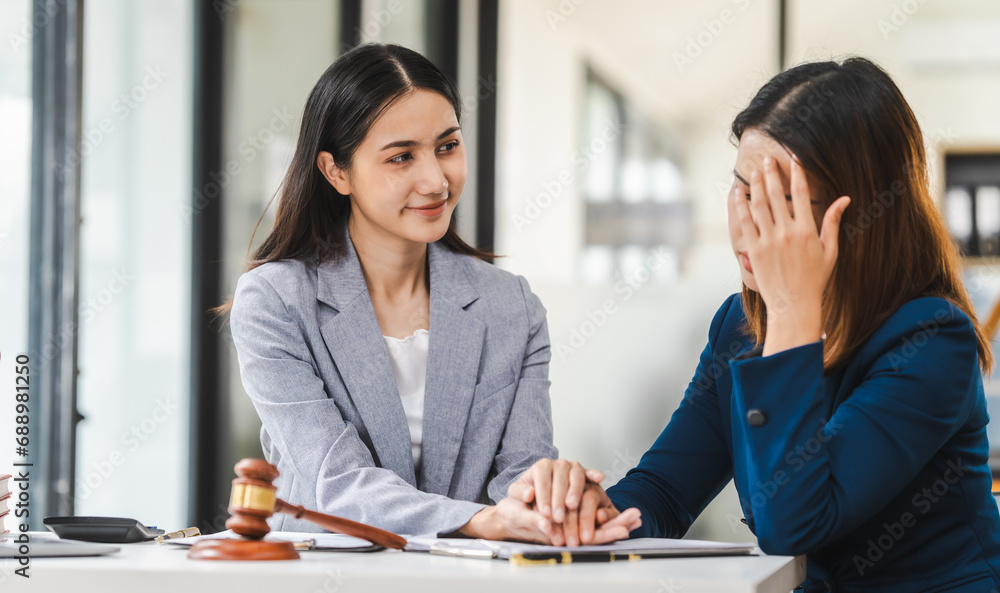 Two middle aged and young Asian lawyer in a formal suit consoles a client during a legal consultation, with a gavel and documents on the table. Two middle aged and young Asian lawyer in a formal suit consoles a client during a legal consultation, with a gavel and documents on the table.