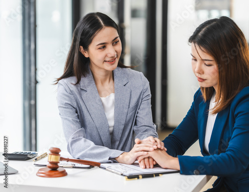 Two middle aged and young Asian lawyer in a formal suit consoles a client during a legal consultation, with a gavel and documents on the table.