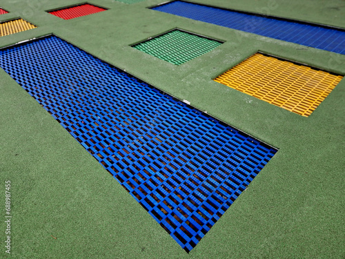 courtyard of school playground, three trampoline jumping mats are sunk below level of a special rubber surface. around are wooden benches attached to the stone walls of a picturesque backyard photo