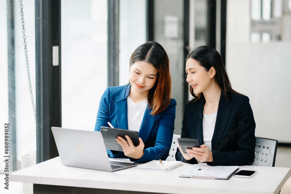 Two Asian businesswoman discuss investment project working and planning strategy with tablet laptop computer Two Asian businesswoman discuss investment project working and planning strategy with tablet laptop computer