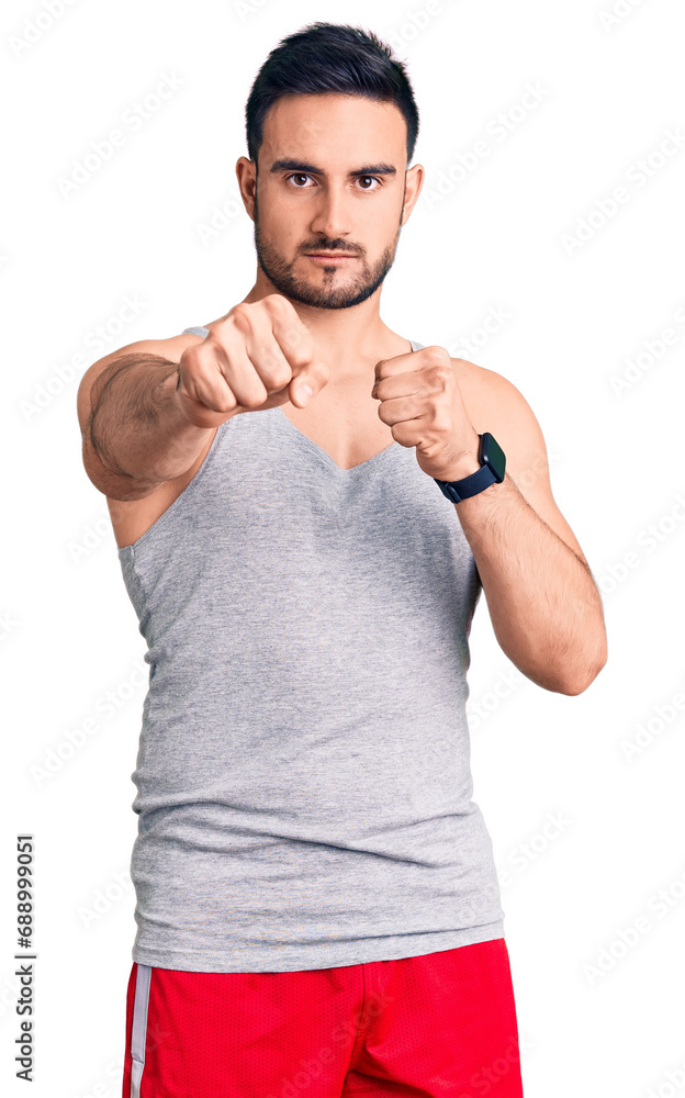 Young handsome man wearing swimwear and sleeveless t-shirt punching fist to fight, aggressive and angry attack, threat and violence Young handsome man wearing swimwear and sleeveless t-shirt punching fist to fight, aggressive and angry attack, threat and violence