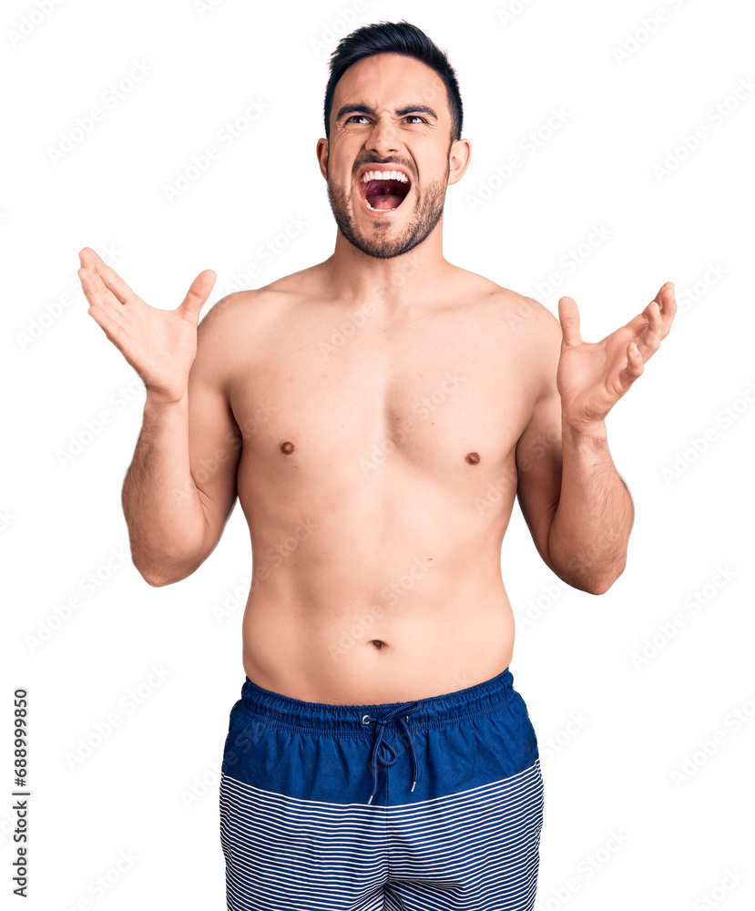 Young handsome man wearing swimwear crazy and mad shouting and yelling with aggressive expression and arms raised. frustration concept. Young handsome man wearing swimwear crazy and mad shouting and yelling with aggressive expression and arms raised. frustration concept.
