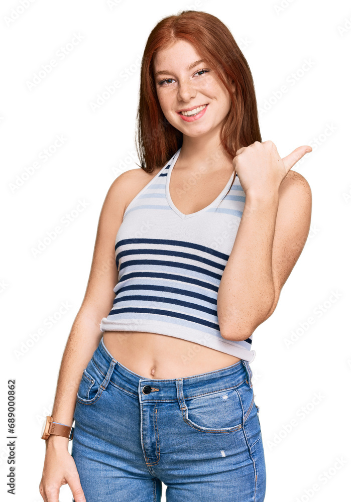 Young read head woman wearing casual clothes smiling with happy face looking and pointing to the side with thumb up. Young read head woman wearing casual clothes smiling with happy face looking and pointing to the side with thumb up.