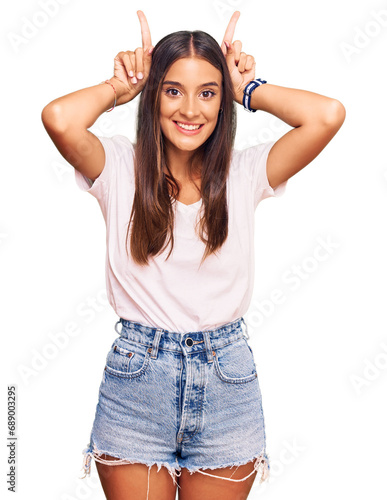 Young hispanic woman wearing casual white tshirt doing funny gesture with finger over head as bull horns © Krakenimages.com