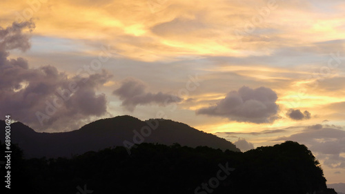 Sunset over the mountains. Sunset over the sea and tropical island. The sun behind the clouds sets below the horizon. The sun's rays color the sky and clouds during sunset.