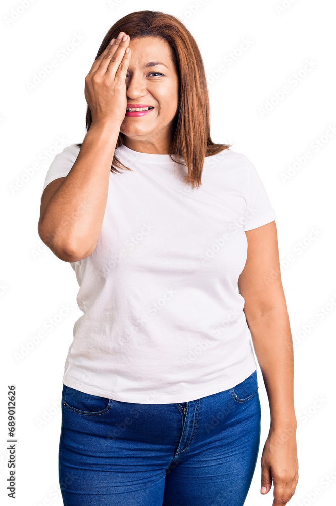 Middle age latin woman wearing casual white tshirt covering one eye with hand, confident smile on face and surprise emotion. Middle age latin woman wearing casual white tshirt covering one eye with hand, confident smile on face and surprise emotion.