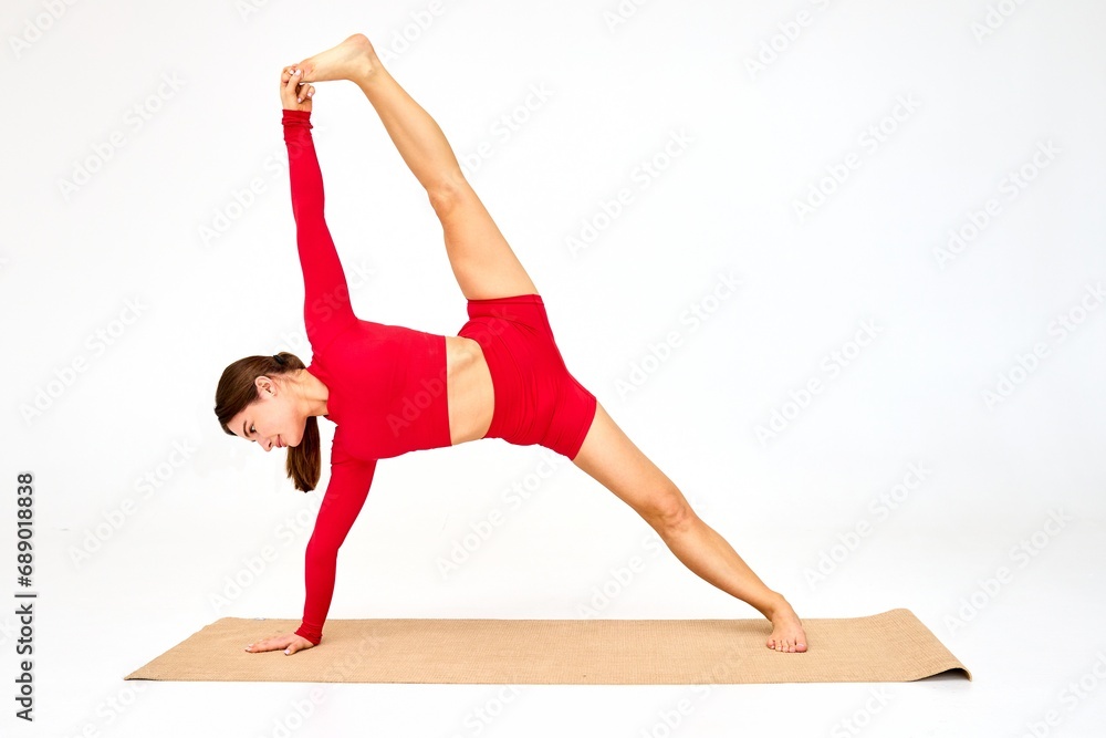 In an inviting indoor space, a yoga coach donning a bold red tracksuit effortlessly showcases flexibility and balance