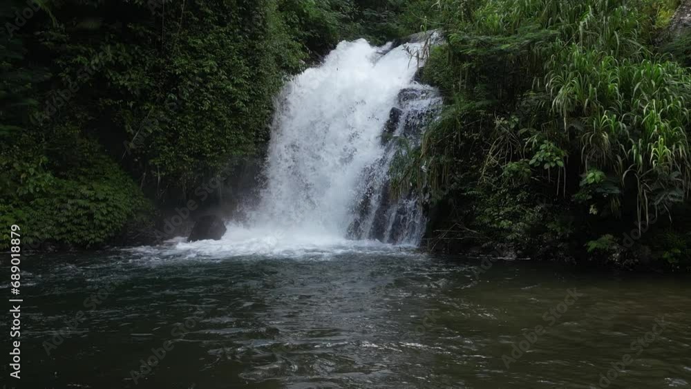 A small, hidden waterfall in the depths of Balinese jungle on a sunny afternoon, aerial. A small, hidden waterfall in the depths of Balinese jungle on a sunny afternoon, aerial.