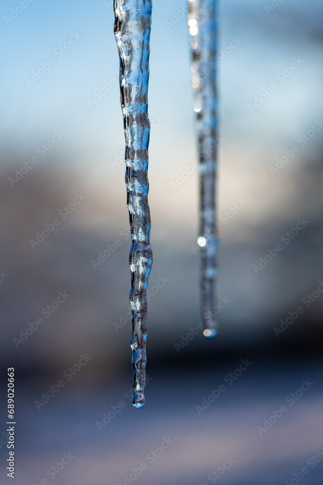 Hanging iciles with dropping water on a very cold winters day with blue sky and bright sunlight in Germany. Close up macro of colorful translucent turquoise blue shapes with blurred background. Hanging iciles with dropping water on a very cold winters day with blue sky and bright sunlight in Germany. Close up macro of colorful translucent turquoise blue shapes with blurred background.