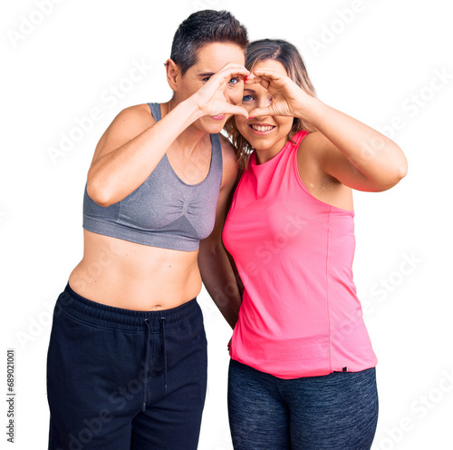 Couple of women wearing sportswear doing heart shape with hand and fingers smiling looking through sign