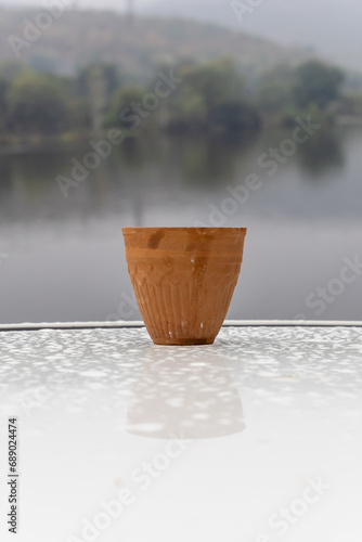 hot tea served in traditional handleless pottery clay cup with blurred mountain lake landscape © explorewithinfo