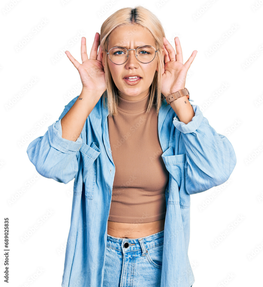 Beautiful young blonde woman wearing glasses trying to hear both hands on ear gesture, curious for gossip. hearing problem, deaf Beautiful young blonde woman wearing glasses trying to hear both hands on ear gesture, curious for gossip. hearing problem, deaf