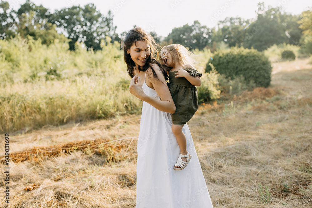 Mother playing with her daughter outdoors in a park on a summer day, laughing.