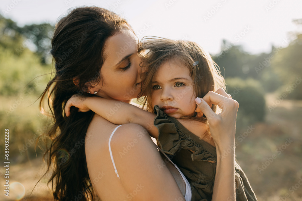 Closeup calm portrait of a mother holding her little sad daughter in arms, outdoors. Closeup calm portrait of a mother holding her little sad daughter in arms, outdoors.